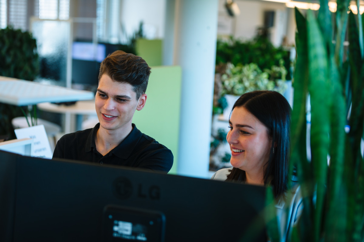 Zwei Personen lächeln vor einem Monitor