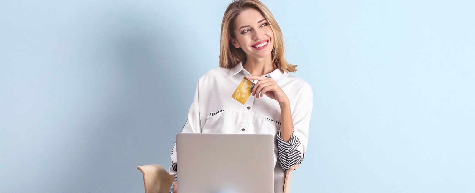 Eine Frau sitzt vor ihrem Laptop mit einer Kreditkarte in der Hand und lächelt.