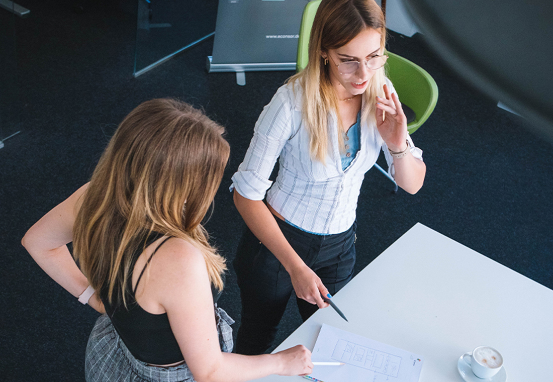 tschuess-besucher-wenn-ihre-einstiegsseite-gleich-die-ausstiegsseite-ist Zwei Frauen stehen an einem Tisch und betrachten gemeinsam einige Papiere.