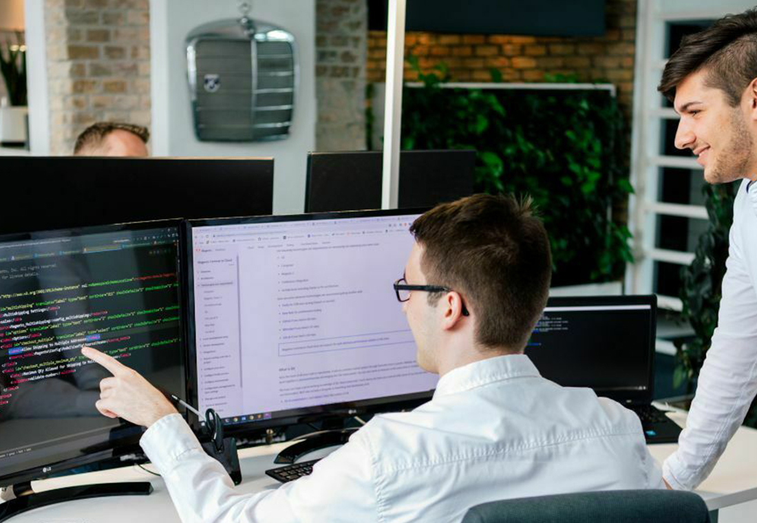 Zwei Männer stehen vor einem Computerbildschirm und betrachten gemeinsam die angezeigten Informationen.