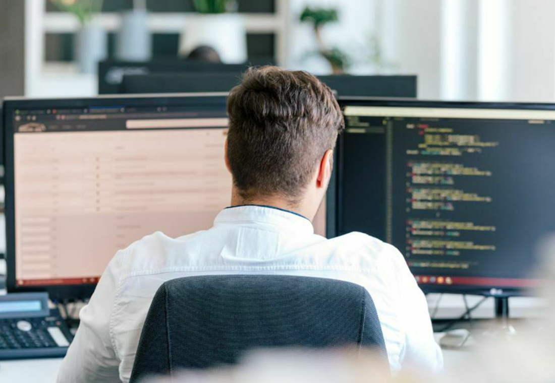 Ein Mann sitzt an einem Schreibtisch mit zwei Computerbildschirmen vor sich.