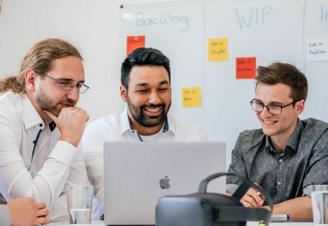 blog_econsor_User-Experience-im-E-Commerce Drei Männer in einem Besprechungsraum, die um einen Laptop versammelt sind und diskutieren.