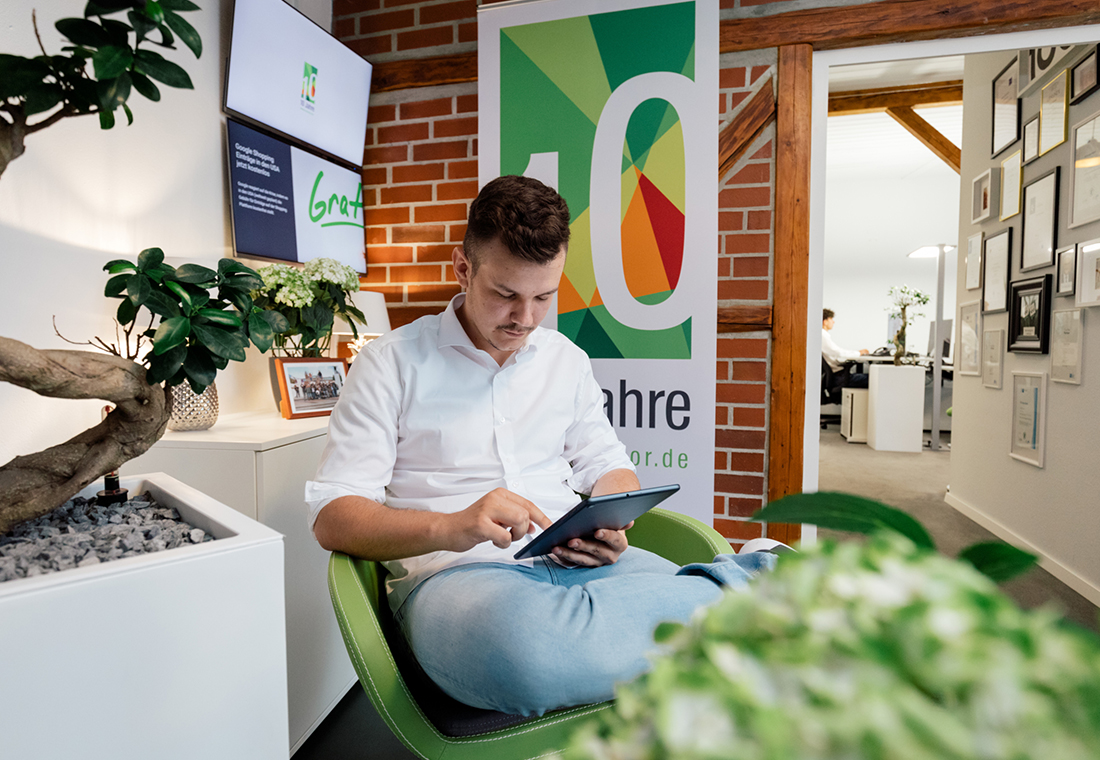Ein Mann sitzt in einem Stuhl und hält ein Tablet in der Hand, während er auf den Bildschirm schaut.