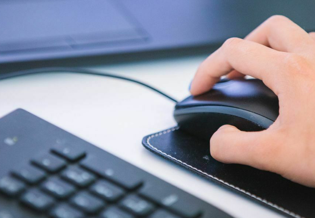 Eine Person steuert einen Computer mit einer Maus, die in der rechten Hand gehalten wird.