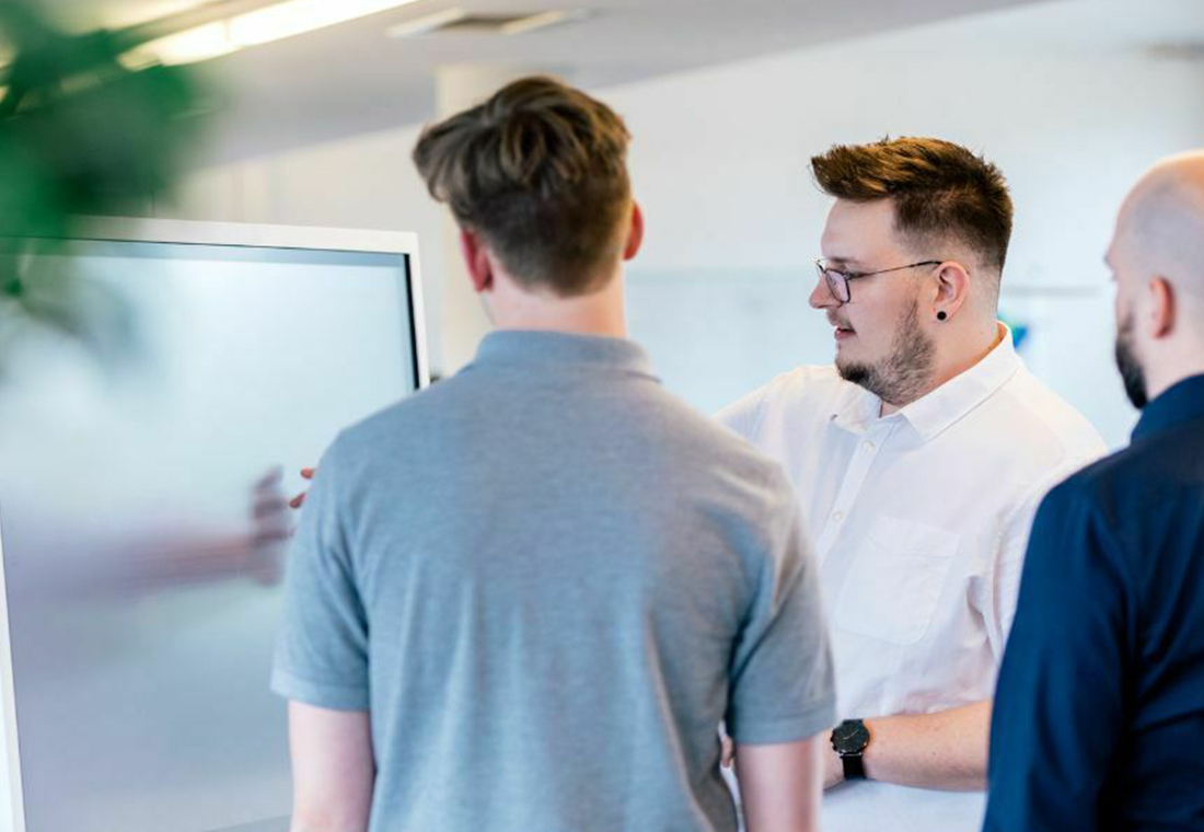 blog-econsor-content-marketing-investitionskosten-einspielen Drei Männer stehen um ein Whiteboard und diskutieren, während sie auf die darauf skizzierten Informationen zeigen.