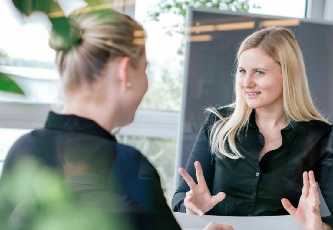 Zwei Frauen führen ein Gespräch an einem Tisch in einem Büro.