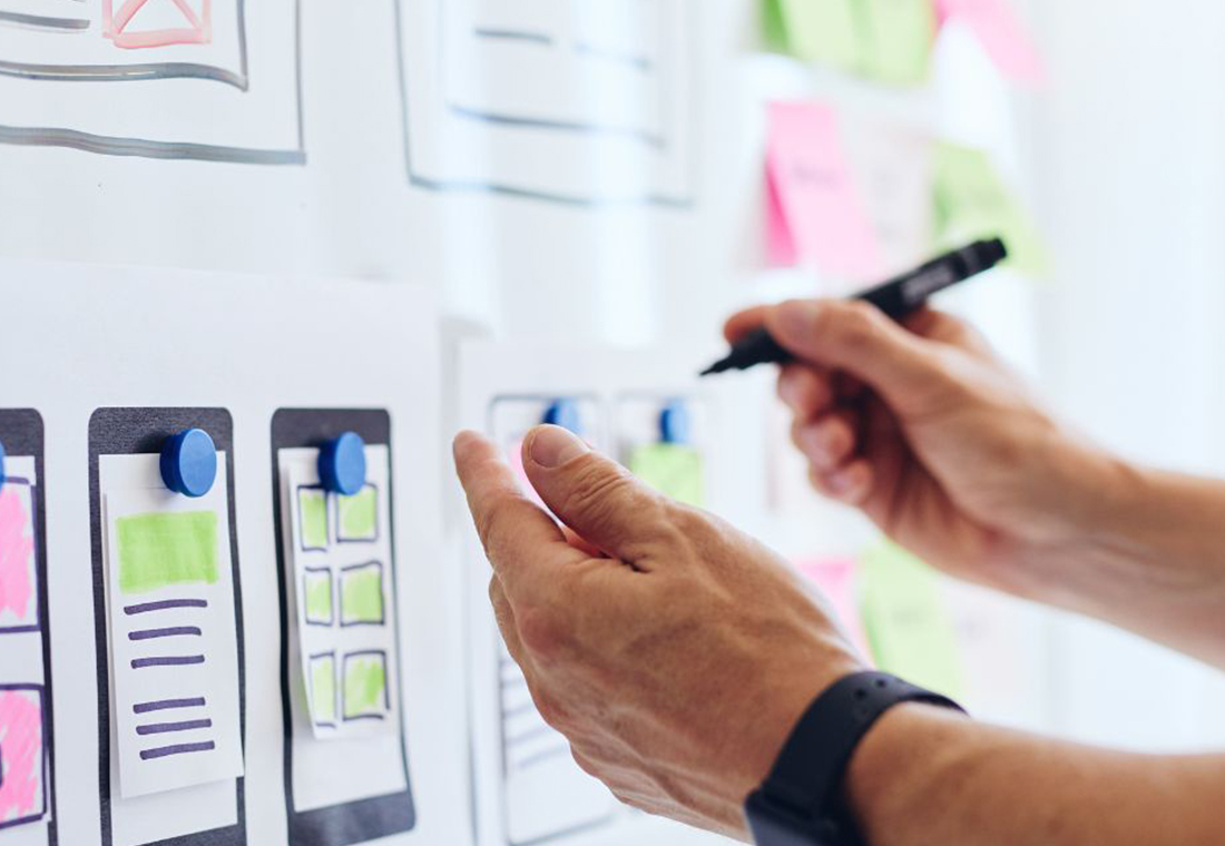 Eine Person schreibt auf ein Whiteboard und verwendet dabei bunte Haftnotizen zur Visualisierung von Ideen.