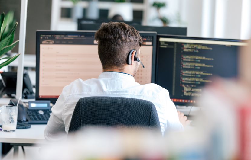 Ein Mitarbeiter sitzt vor zwei Bildschirmen und arbeitet