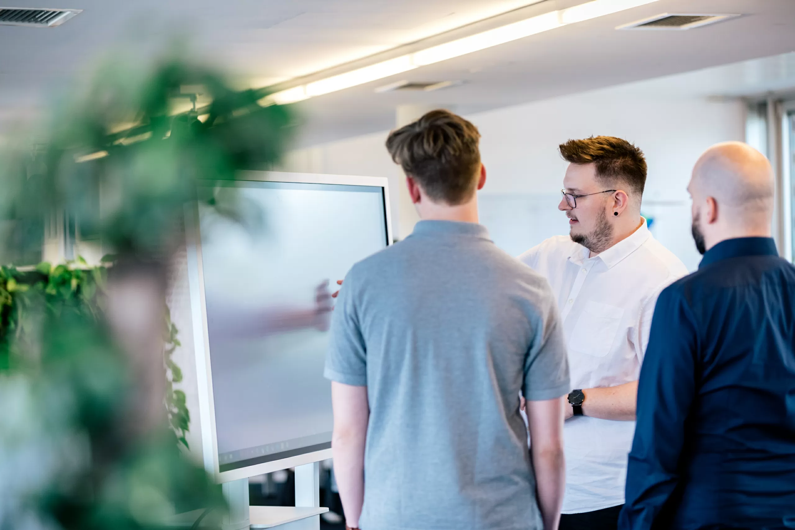 Drei Mitarbeitende besprechen etwas vor einem Whiteboard