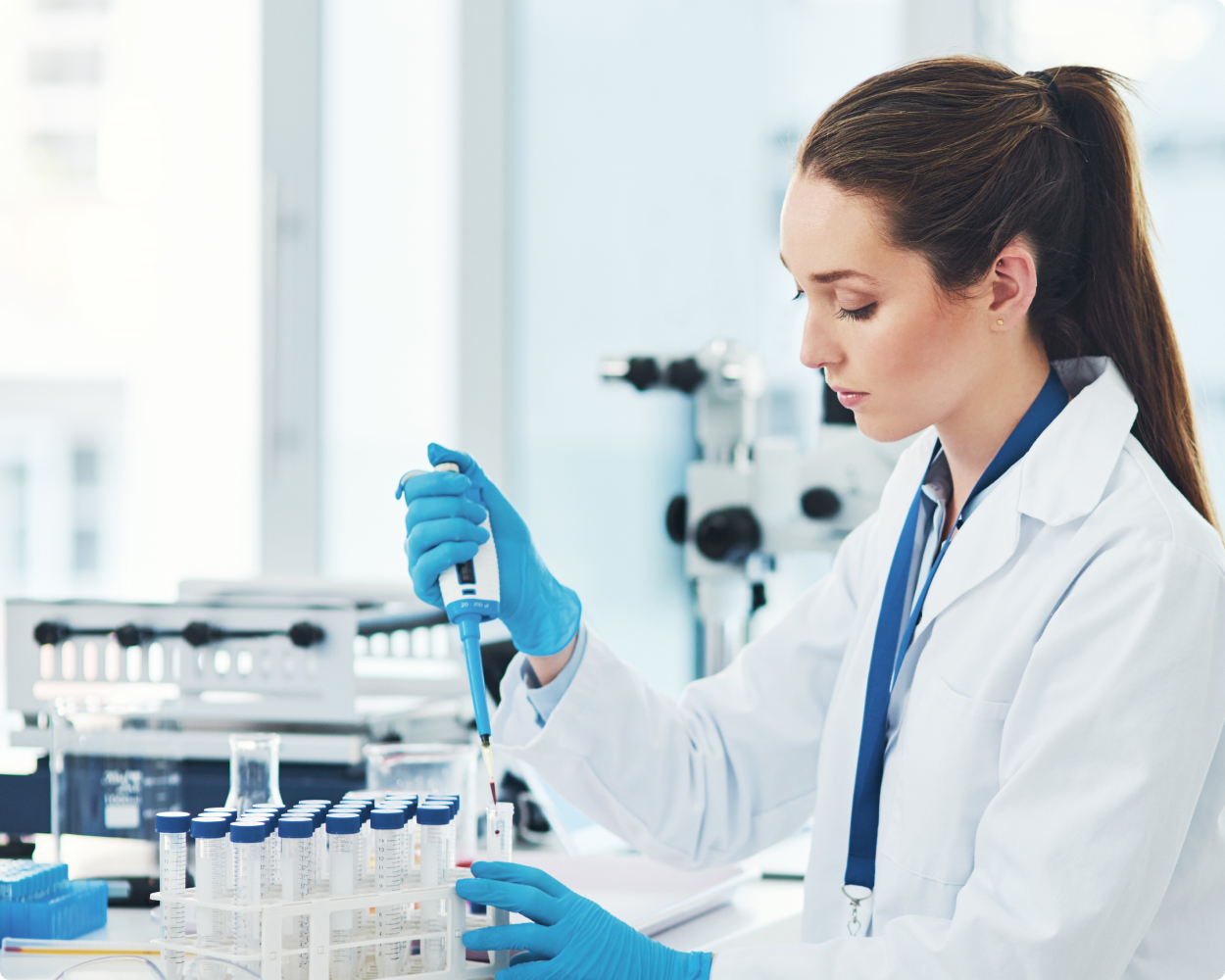 Eine Laborantin befüllt mit einer Pipette Reagenzgläser von ahf und trägt dabei einen Kittel und Handschuhe.