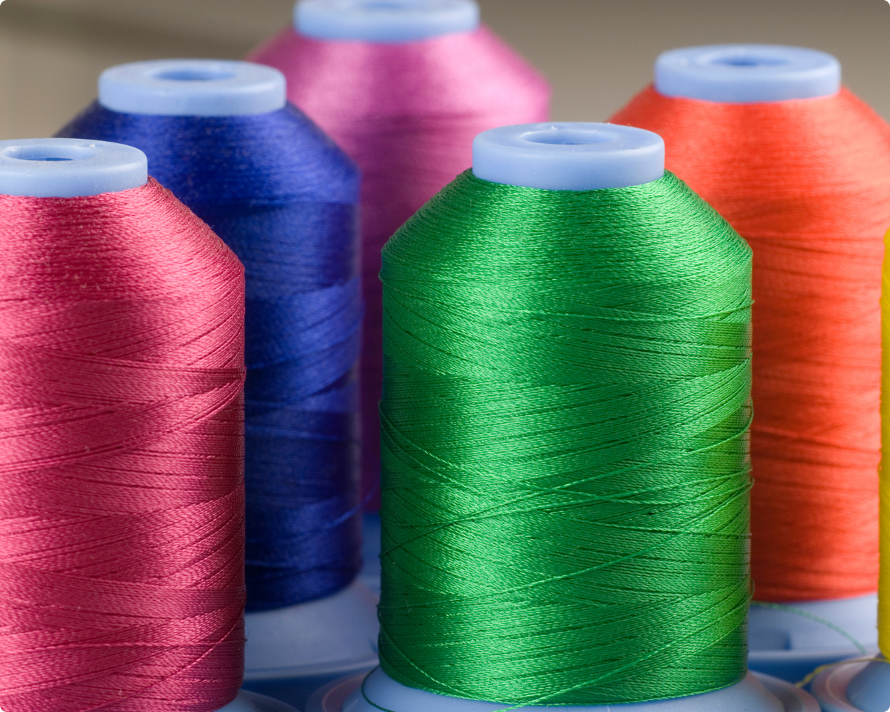 Fünf verschiedene Spulen mit Amann Nähgarn in den Farben grün, orange, pink, blau und grün.