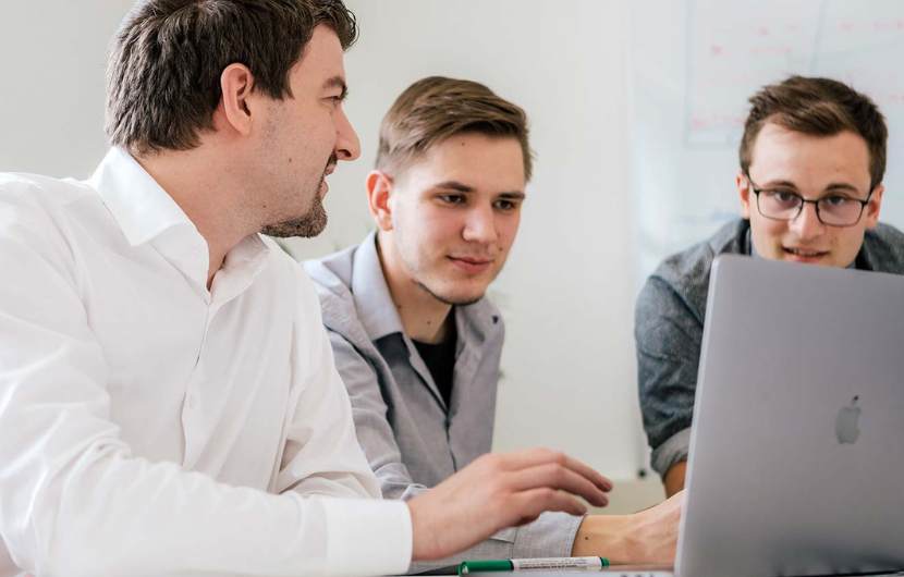 Drei Männer sitzen vor einem Computer und besprechen sich