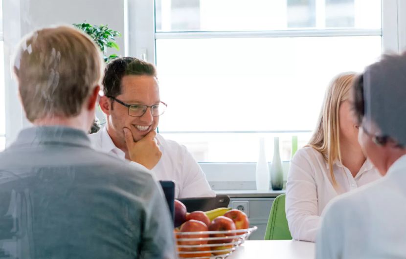 Zwei Mitarbeiterinnen sitzen an einem Tisch, wobei eine auf einen Laptop zeigt und mit der anderen spricht. Beide tragen schwarz und arbeiten an einer CMS-Lösung.