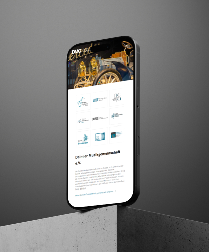 daimler-bilderreihe-1 Ein Smartphone steht hochkant auf einer Steinoberfläche. Auf dem Bildschirm des Smartphones ist die DMG-Website abgebildet.