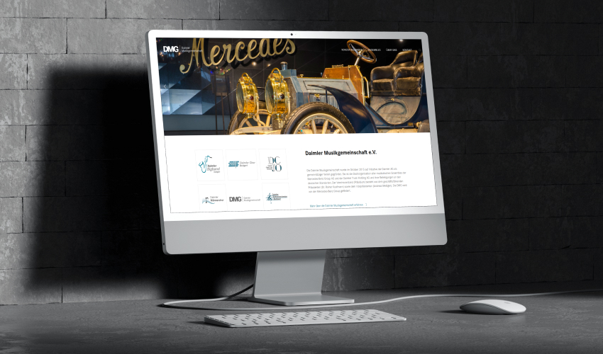 daimler-bilderreihe-2 Ein Monitor steht auf einem grauen Tisch. Auf dem Bildschirm des Monitors ist die DMG-Website abgebildet.