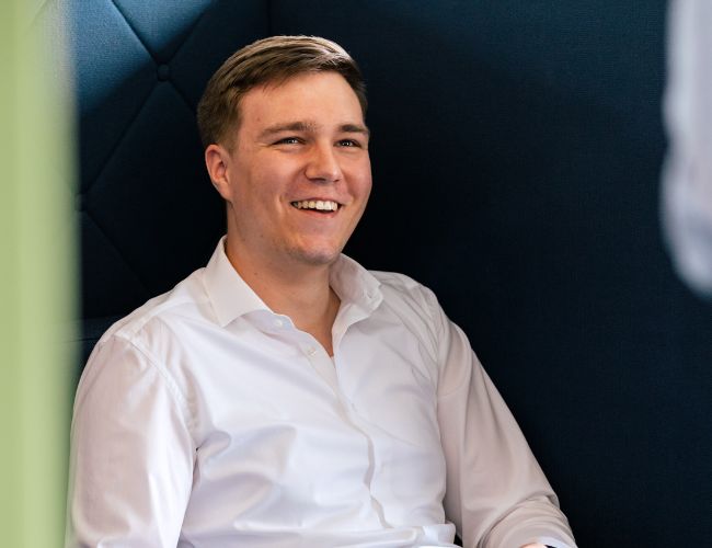 E-Commerce und Portalentwicklung bei ECONSOR Ein junger Mann sitzt in einem modernen Büro, lächelt und wirkt entspannt, während er an einem E-Commerce-Portalprojekt arbeitet.