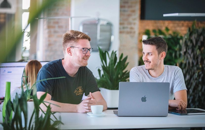 Zwei Kolleg:innen in einem Besprechungsraum erörtern Details für ein individuelles Webportal für Ihr Unternehmen – maßgeschneiderte Programmierlösungen inklusive.