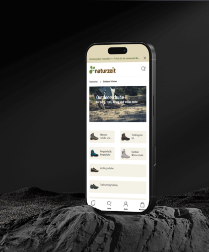 Ein Smartphone steht hochkant auf einem düsteren und unebenem Stein. Auf dem Bildschirm des Smartphones ist der naturzeit-Shop abgebildet.