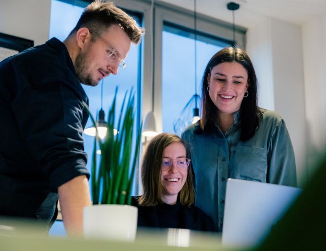 Onlineberatung: Strategisch & Transparent Drei Mitarbeitende der ECONSOR Digitalagentur stehen in einem modernen Büro um einen Laptop und diskutieren strategische Onlineberatung für Unternehmen – individuell und praxisnah für KMU & Konzerne.