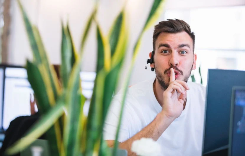 Ein Mitarbeiter im Büro, der dass "Leise-Zeichen" mit seiner Hand nachahmt