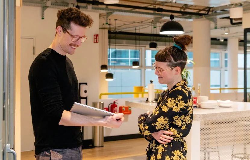 Zwei Mitarbeiter schauen gemeinsam auf ein Tablet und lächeln dabei.