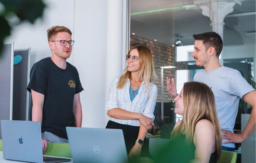 Vier Kolleginnen und Kollegen besprechen eine Online-Marketing-Konzeption an Laptops in einem modernen Büro