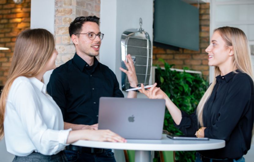 Drei ECONSOR-Mitarbeiter stehen um einen Tisch mit Laptop und besprechen ein Kundenprojekt – die Szene illustriert dynamische Teamarbeit in einer modernen Online-Marketing-Agentur.