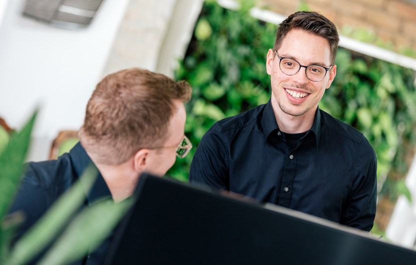 Zwei Mitarbeiter besprechen sich an ihrem Arbeitsplatz in der Magento-Agentur
