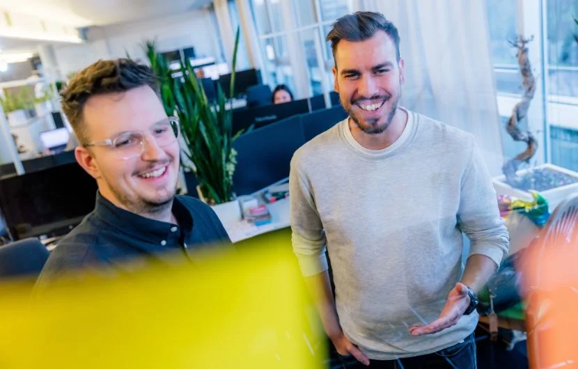 SEO-Agentur in Berlin Zwei Mitarbeiter betrachten Post IT's, die an einer durchsichtigen Glaswand befestigt sind und lächeln.