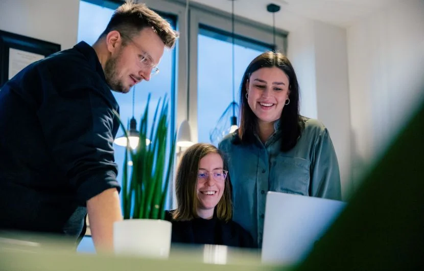 Ihre SEO-Agentur in Köln Drei Mitarbeiter lächeln und sprechen miteinander während sie auf eine Laptopbildschirm schauen.