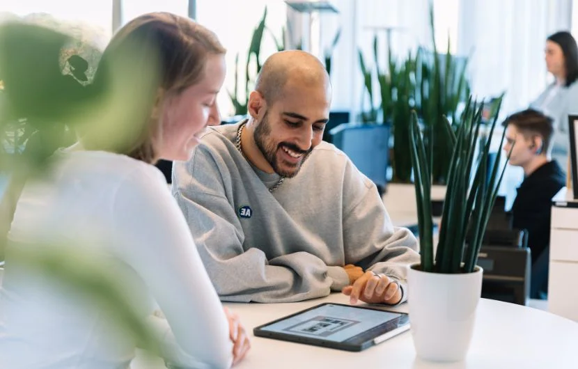 Ihre SEO-Agentur in Mannheim Zwei Kollegen lächeln und schauen dabei auf ein Tablet, dass ein Kundenwebdesign zeigt