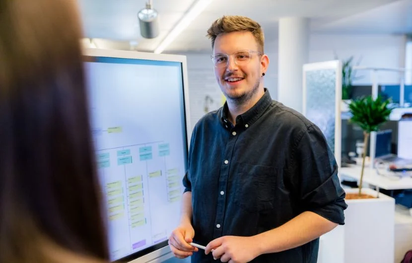 Ihre SEO-Agentur in Stuttgart Ein Mitarbeiter lächelt und stellt vor einem Whiteboard eine Präsentation vor.