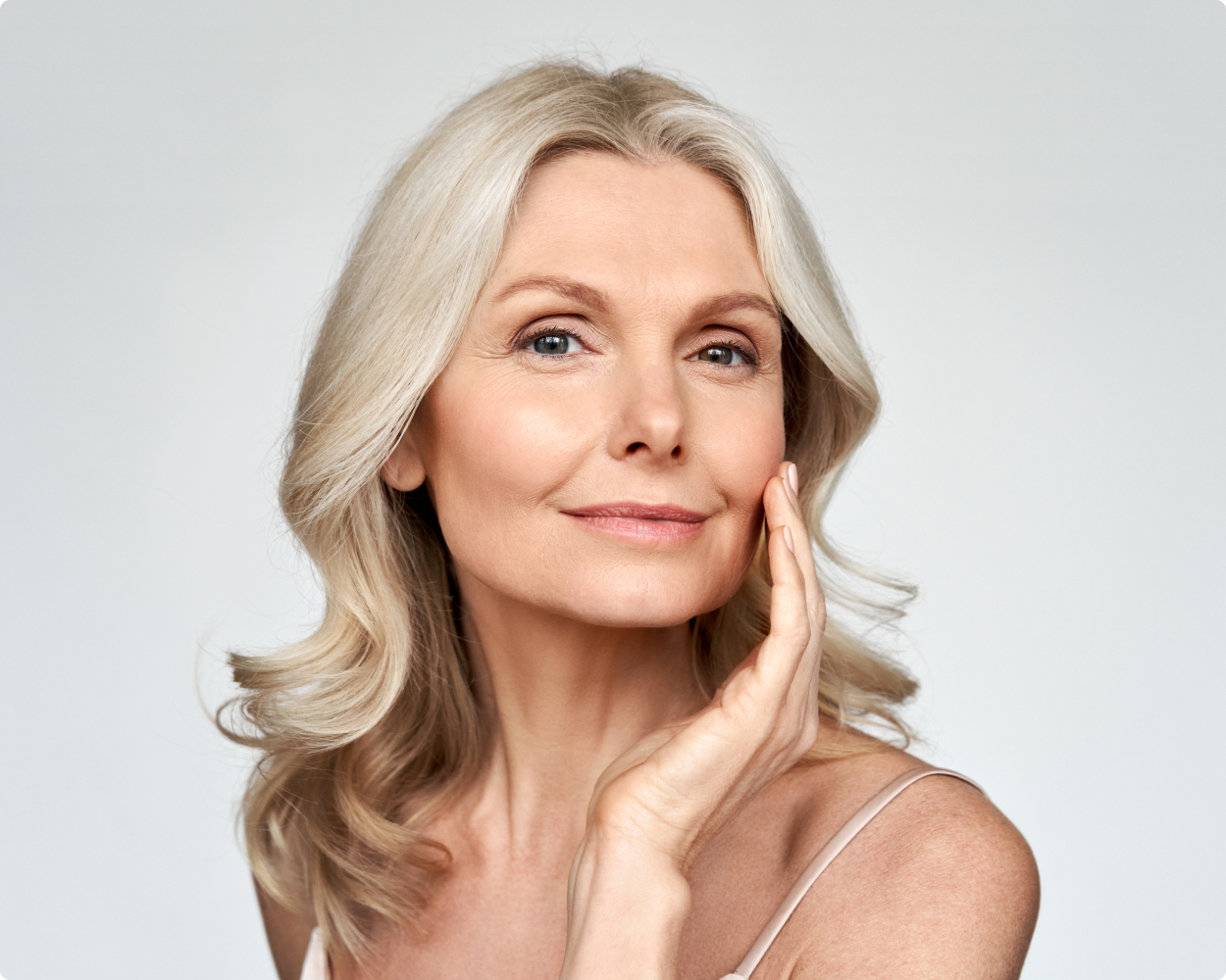 Ältere Dame berührt sich mit einer Hand im Gesicht Sophienklinik Eine ältere Dame berührt mit einer Hand ihr Gesicht, während sie dabei direkt in die Kamera schaut während sie über ihren kosmetischen Eingriff in der Sophienklinik nachdenkt