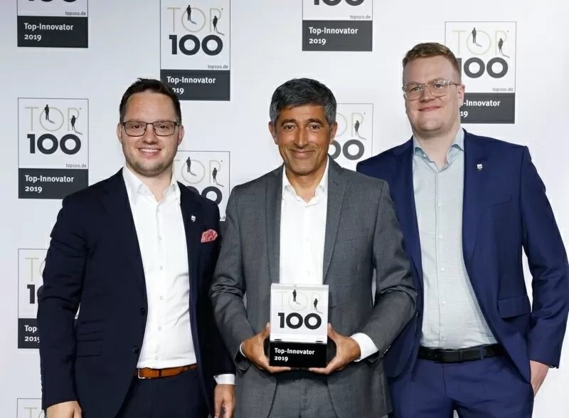 Drei Männer stehen mit einer Auszeichnung vor einer Leinwand