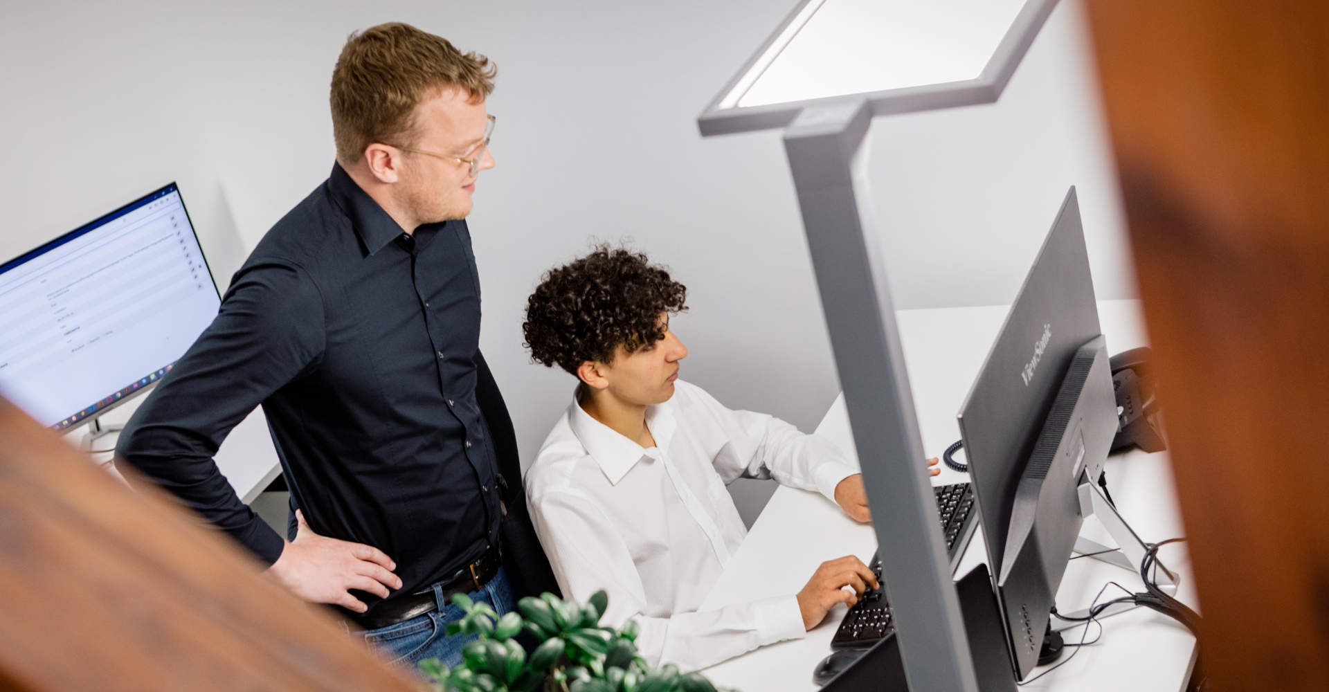 typo3-heidelberg Ein Auszubildender arbeitet am Schreibtisch, während der Chef ihn begleitet.