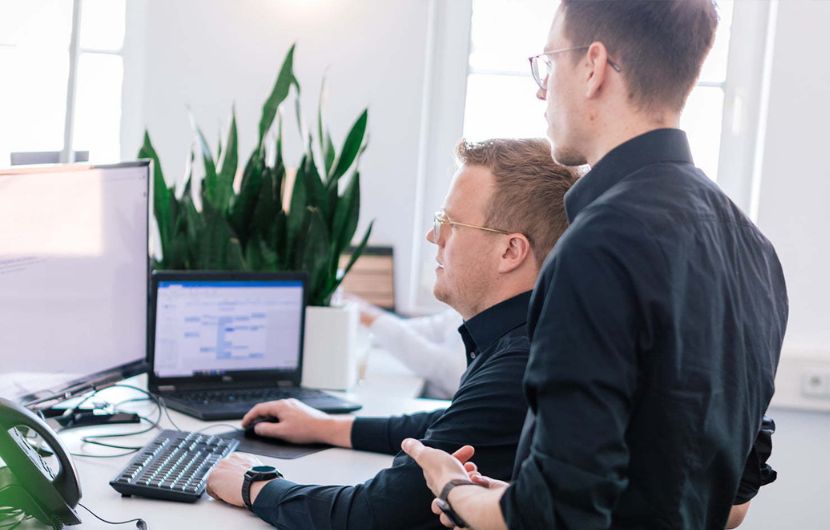 Zwei Mitarbeiter besprechen sich an ihrem Arbeitsplatz in der TYPO3-Agentur