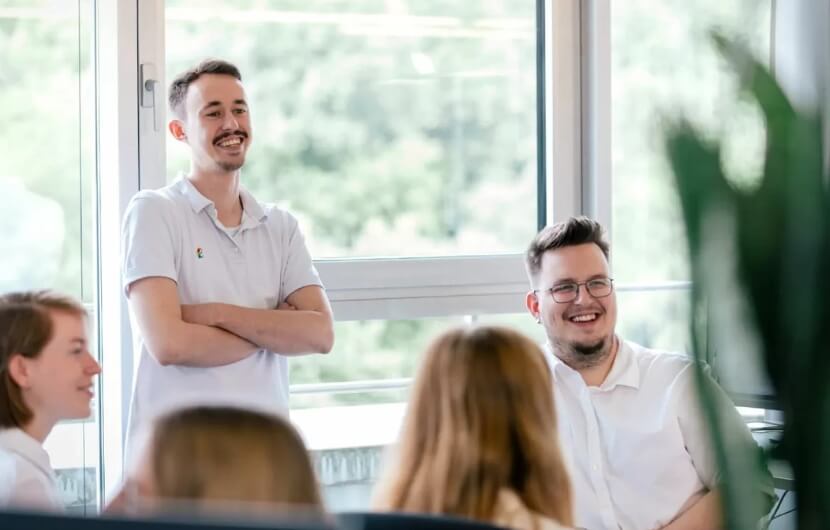 Ihre Webdesign-Agentur in Frankfurt In einer Besprechung einer Webdesign-Agentur unterhalten sich mehrere junge Mitarbeitende gut gelaunt in einem modernen, hellen Büro mit großen Fenstern.