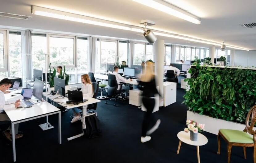 In der offenen und modern gestalteten Bürofläche einer Webdesign-Agentur arbeiten Mitarbeitende an ihren Projekten, während eine Person dynamisch durch den Raum geht.