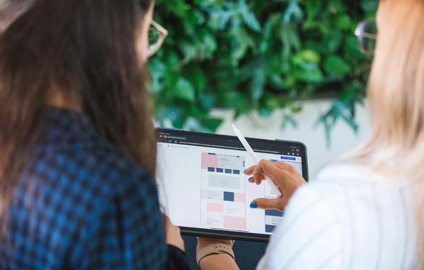 Zwei Mitarbeiterinnen schauen auf ein Tablet, während eine Mitarbeiterin ein Wireframe zeigt