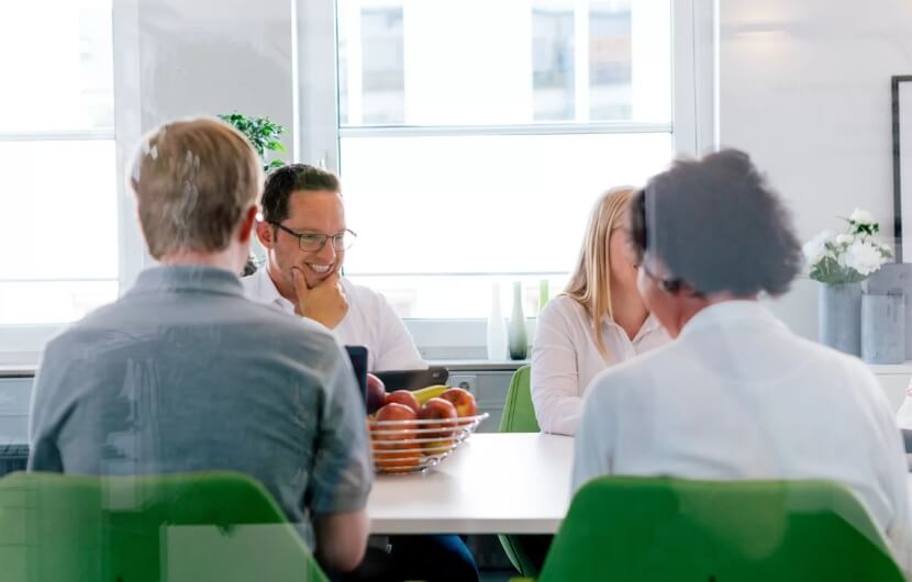 Vier Mitarbeiter sitzen in einem Besprechungsraum und zwei davon lächeln
