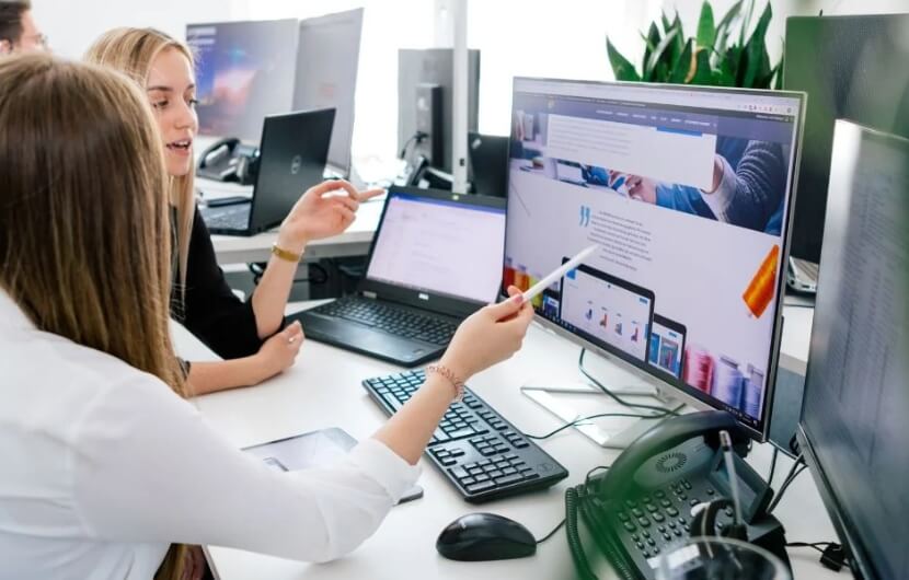 webdesign-agentur-nuernberg In einer Besprechung einer Webdesign-Agentur besprechen zwei Mitarbeiterinnen gemeinsam die Gestaltung einer Webseite an einem großen Bildschirm.