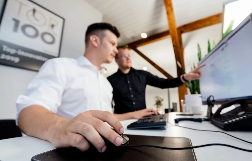 Ein Teammitglied bespricht vor dem Display Design‑ und Entwicklungsfragen eines Webportals – vereint technische Umsetzung und nutzerzentriertes Design.