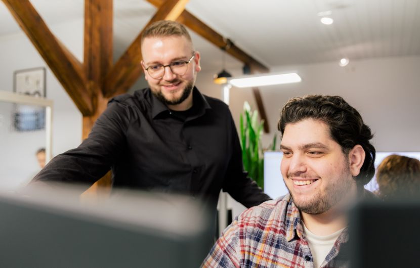 Zwei Entwickler stehen an Bildschirmen in einem modernen Büro und diskutieren gemeinsam die Webportal‑Entwicklung und individuelle Programmierlösungen.