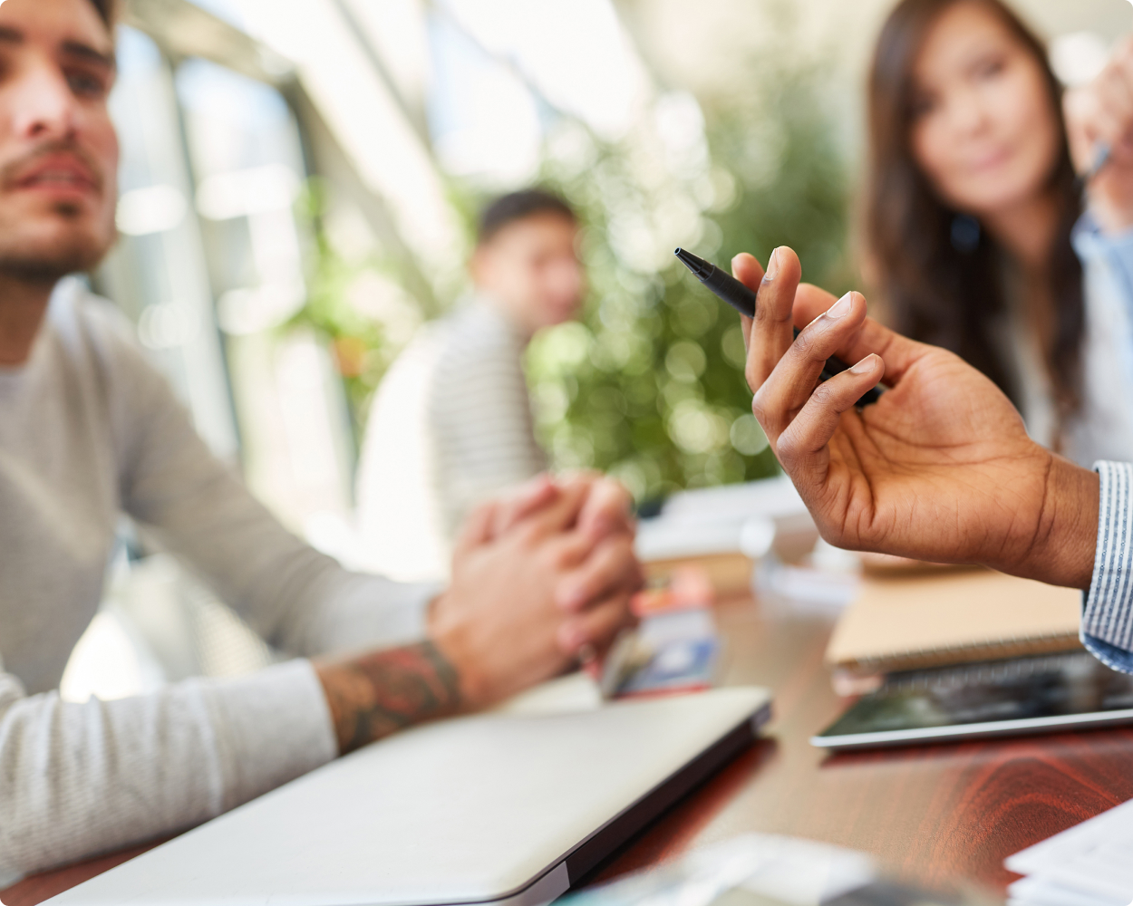 Vier Personen sitzen an einem gemeinsamen Tisch und schauen. Drei davon schauen auf die Person, die gerade redet und etwas von Wolters Kluwer präsentiert und seine Hand hebt und in dieser einen Kugelschreiber hält.
